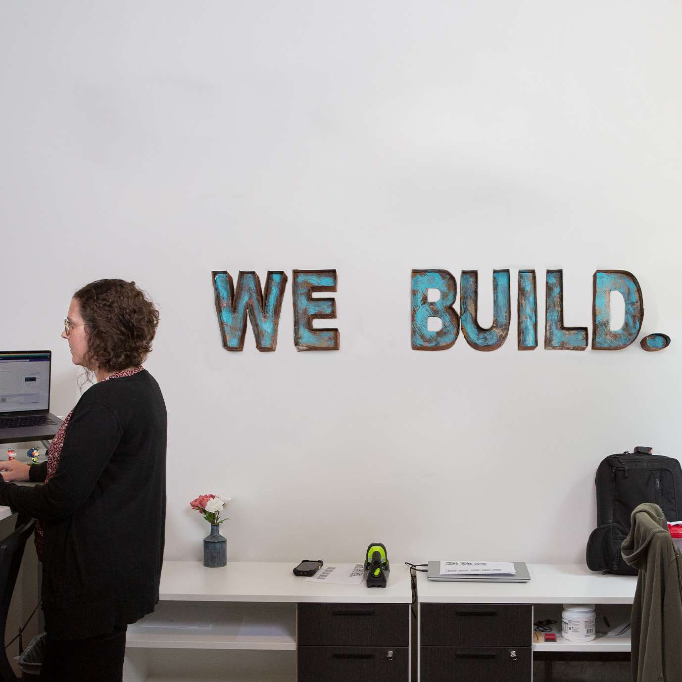 Woman working at a standing desk with We Build sign in the background