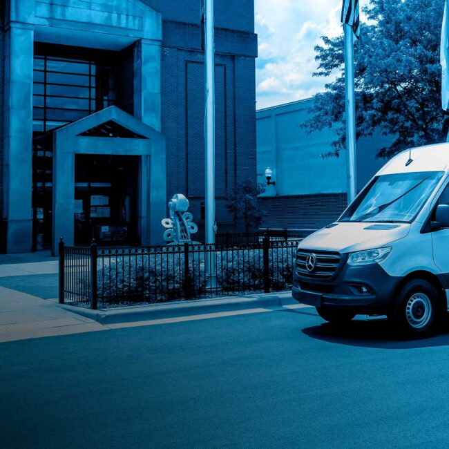 A package delivery worker carrying a box out of the side door of a utility van parked on a city street