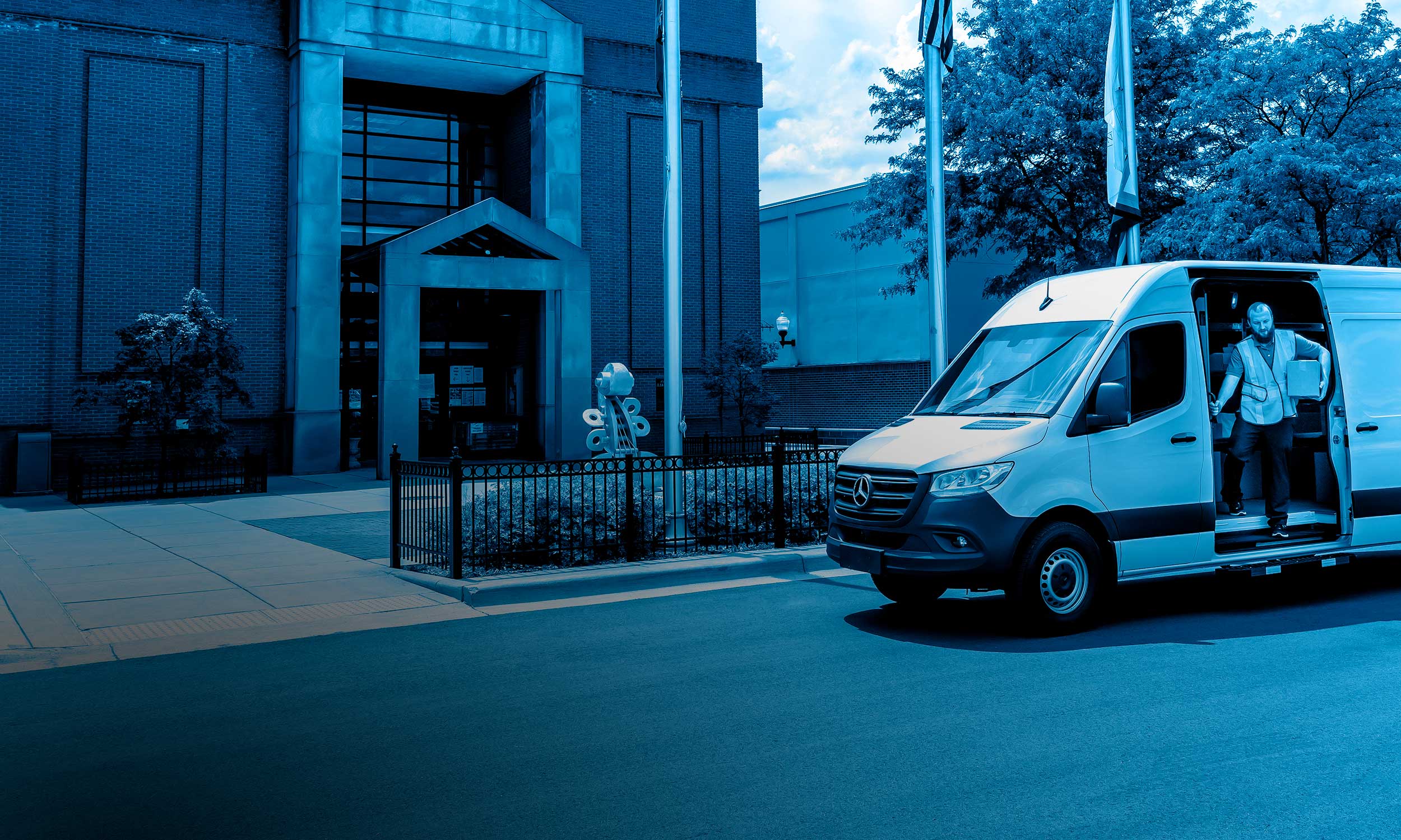 A package delivery worker carrying a box out of the side door of a utility van parked on a city street