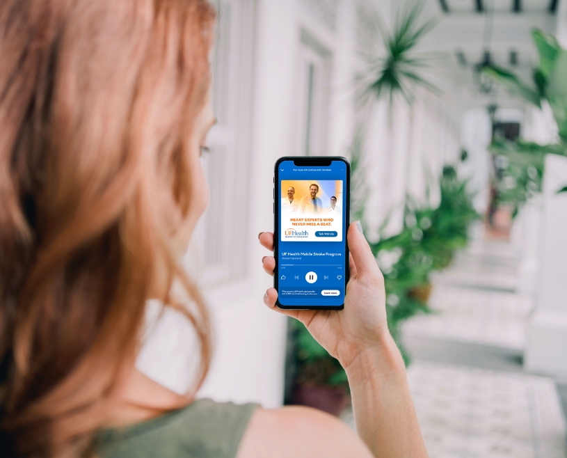 Woman looking at cell phone with UF Health digital audio playing on screen