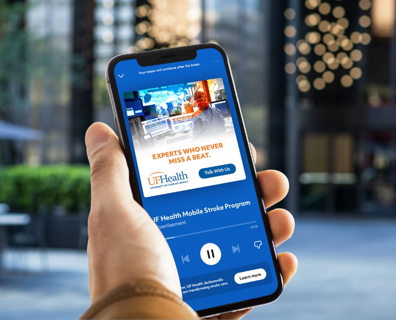 Close up of hand holding a phone with UF Health digital audio playing on screen